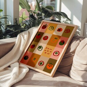 May include: A framed print featuring a grid of colorful tomato illustrations in red, green, and orange. The word "POMODORO" is printed in the center. The artwork has a light wooden frame and is displayed on a sofa.