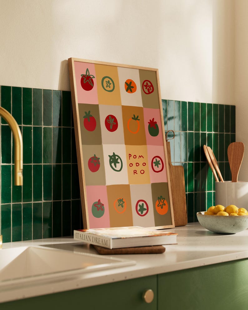 May include: A framed art print featuring a grid of colorful tomato illustrations. The artwork includes the word "POMODORO" and is set against a backdrop of pink, beige, and brown squares. The frame is made of light-colored wood.