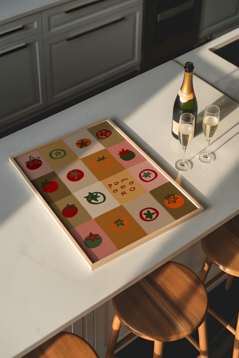 May include: A framed artwork featuring a grid of colorful squares with tomato illustrations and the word "POMODORO". A bottle of champagne and two filled glasses sit nearby. The artwork is on a white countertop.
