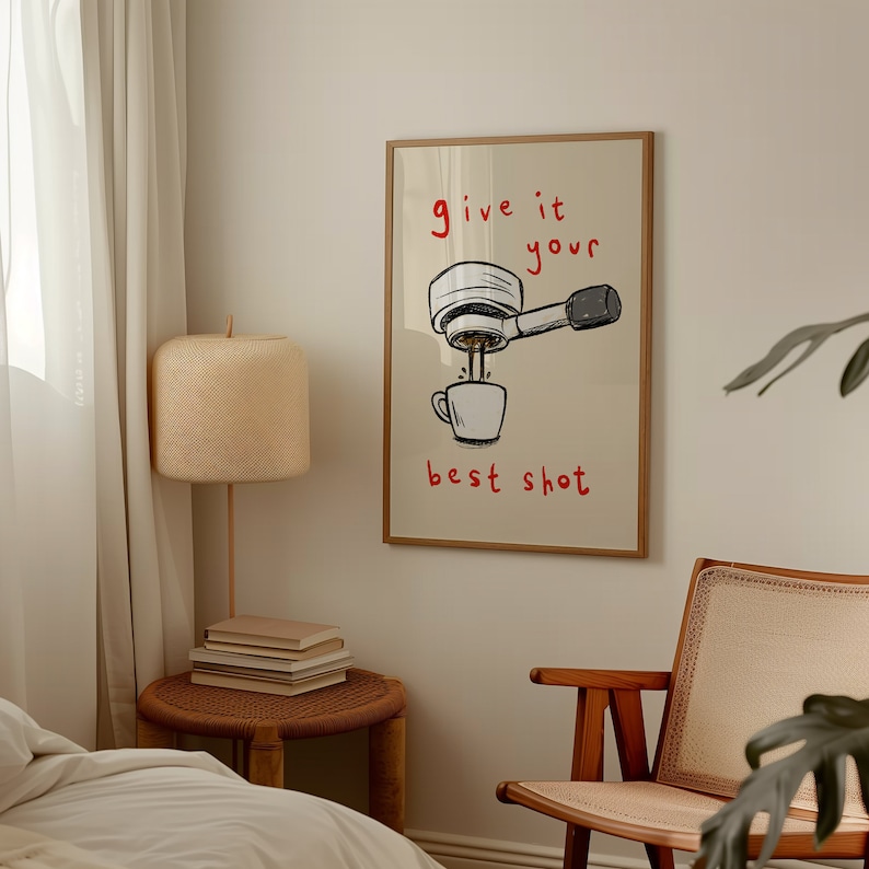 以下が含まれることがあります： コーヒーマシンのイラストと赤い文字「give it your best shot」が描かれたフレーム入りのプリント。白いマグカップにコーヒーが注がれる様子が描かれています。木製のフレームに入っており、ニュートラルな色調の部屋に飾られています。