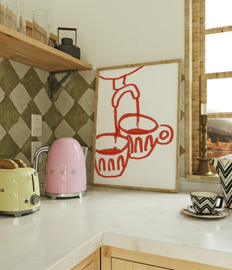 May include: A pink electric kettle and a yellow toaster on a white countertop. A framed illustration of two red cups with a red faucet pouring liquid into the cups hangs on the wall behind the appliances.