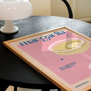 Peut inclure: Une affiche encadr&eacute;e avec un fond rose et une illustration bleue et blanche d'un cocktail margarita. Le texte "margarita" est en lettres bleues et blanches. Les ingr&eacute;dients sont list&eacute;s sous l'illustration&nbsp;: 1&nbsp;oz de Cointreau, 1&nbsp;oz de jus de citron vert, 2&nbsp;oz de tequila. Le mot "COCKTAIL" est en lettres bleues en bas de l'affiche.