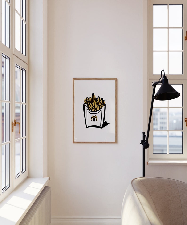 K&ouml;nnte beinhalten: Ein gerahmter Druck einer Schwarzwei&szlig;illustration eines gelben Pommes-Beh&auml;lters mit dem Buchstaben "M" darin. Der Hintergrund ist wei&szlig;.
