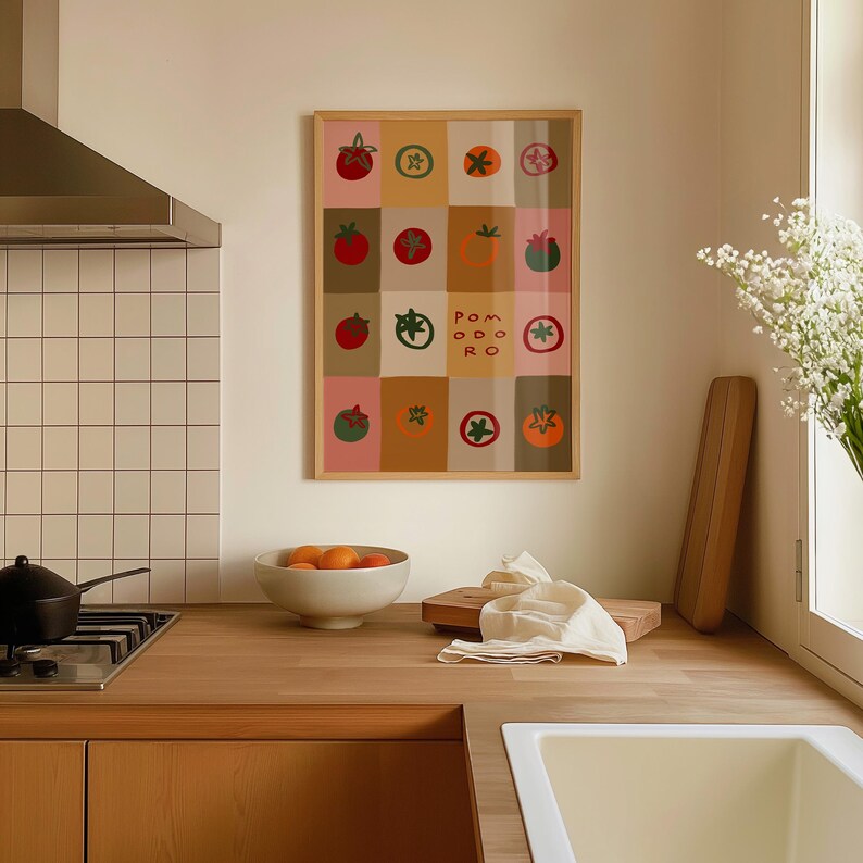 May include: A framed art print featuring a grid of colorful tomato illustrations. The artwork includes various tomato designs and the word "Pomodoro". The print is displayed in a kitchen setting with a wooden countertop and a bowl of oranges.