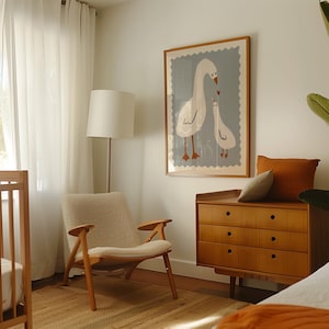 K&ouml;nnte beinhalten: Ein helles Kinderzimmer mit einem gerahmten Druck von zwei G&auml;nsen, einer Holzkommode, einem gem&uuml;tlichen Stuhl und einem Kinderbett. Das Kunstwerk zeigt eine Muttergans und ein G&auml;nsek&uuml;ken mit einem Herz. Der Raum hat eine neutrale Farbpalette mit warmen Holzt&ouml;nen.