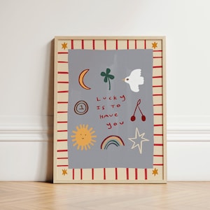 May include: A framed print with a gray background and red and white stripes. The print features a variety of illustrations including a sun, a rainbow, a four-leaf clover, a bird, a cherry, a star, and a circle with the number one. The text "Lucky is to have you" is written in red.