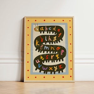 May include: A framed wall art print featuring a long, dark green caterpillar winding in an S-shape across a light gray background. The caterpillar's body is decorated with the lowercase alphabet letters a through z in various bright colors.