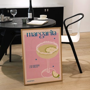 Peut inclure: Une affiche rose et blanche avec le texte "margarita" en bleu et blanc. L'affiche pr&eacute;sente un verre &agrave; cocktail avec une margarita, un quartier de citron vert et un motif d'&eacute;toile. La recette d'une margarita est indiqu&eacute;e sous l'image&nbsp;: 1&nbsp;oz de Cointreau, 1&nbsp;oz de jus de citron vert, 2&nbsp;oz de tequila. L'affiche comprend &eacute;galement le texte "Cocktail 01".
