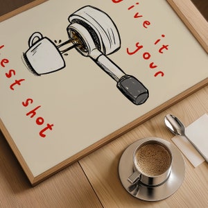 以下が含まれることがあります： コーヒーをテーマにした額入りのプリント。アートワークは、赤い文字で「Give it your best shot」と書かれた、カップにコーヒーを注ぐポルタフィルターのスケッチが特徴です。ソーサーに乗ったコーヒーカップとスプーンがテーブルにあります。