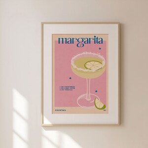 Peut inclure: Une affiche rose et blanche avec le texte "margarita" en bleu et blanc. L'affiche repr&eacute;sente un verre de margarita avec un quartier de citron vert et un fond rose. Le texte "cocktail" est en bas de l'affiche.