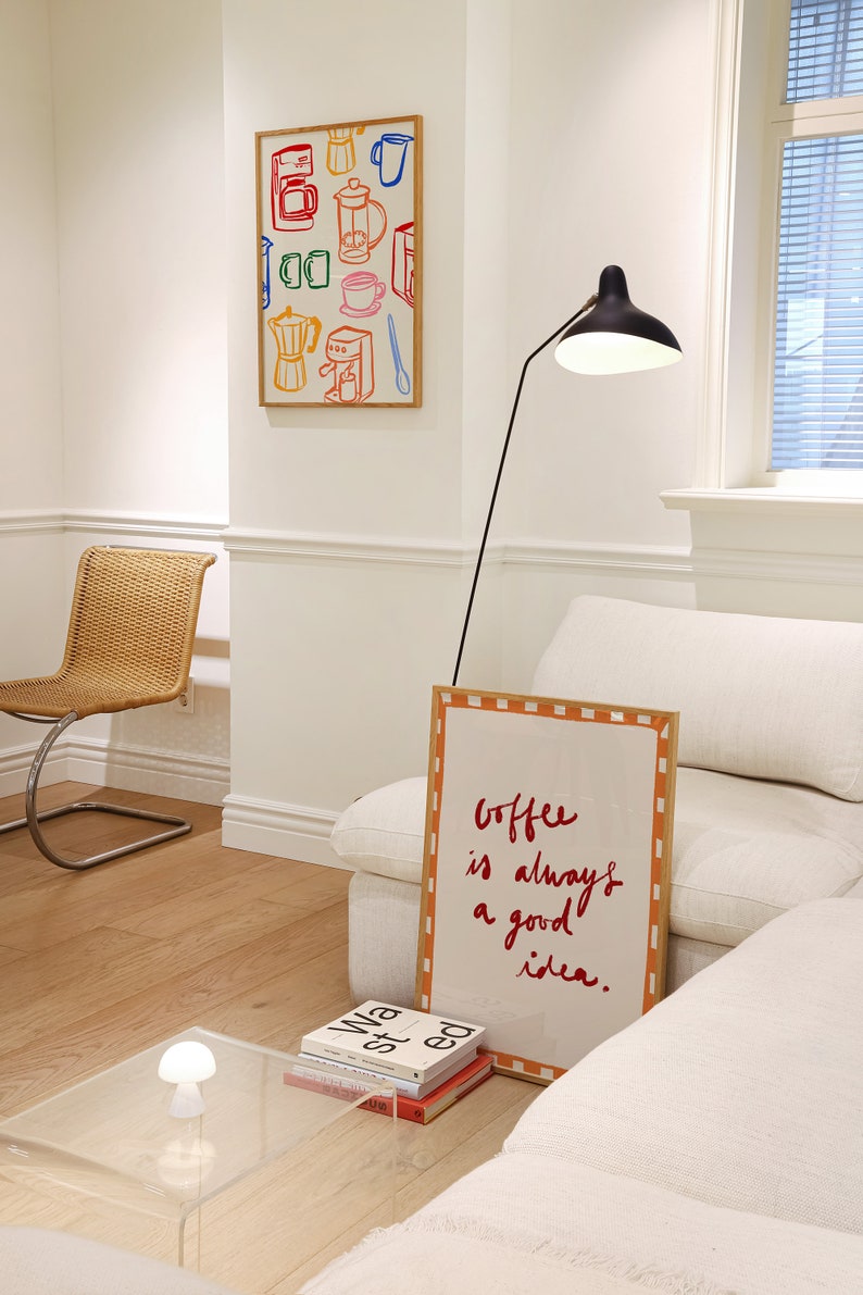 May include: A white couch with a throw pillow and a framed sign that reads "Coffee is always a good idea."  A black floor lamp with a white shade is next to the couch. A small table with a white lamp and a stack of books is in the foreground.