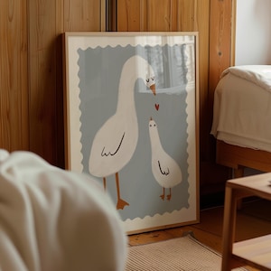 K&ouml;nnte beinhalten: Gerahmter Kunstdruck mit einer skurrilen Illustration von zwei wei&szlig;en G&auml;nsen mit orangefarbenen Beinen und Schn&auml;beln vor einem hellblauen Hintergrund. Ein kleines rotes Herz befindet sich zwischen den G&auml;nsen. Das Kunstwerk ist in einem Holzrahmen.