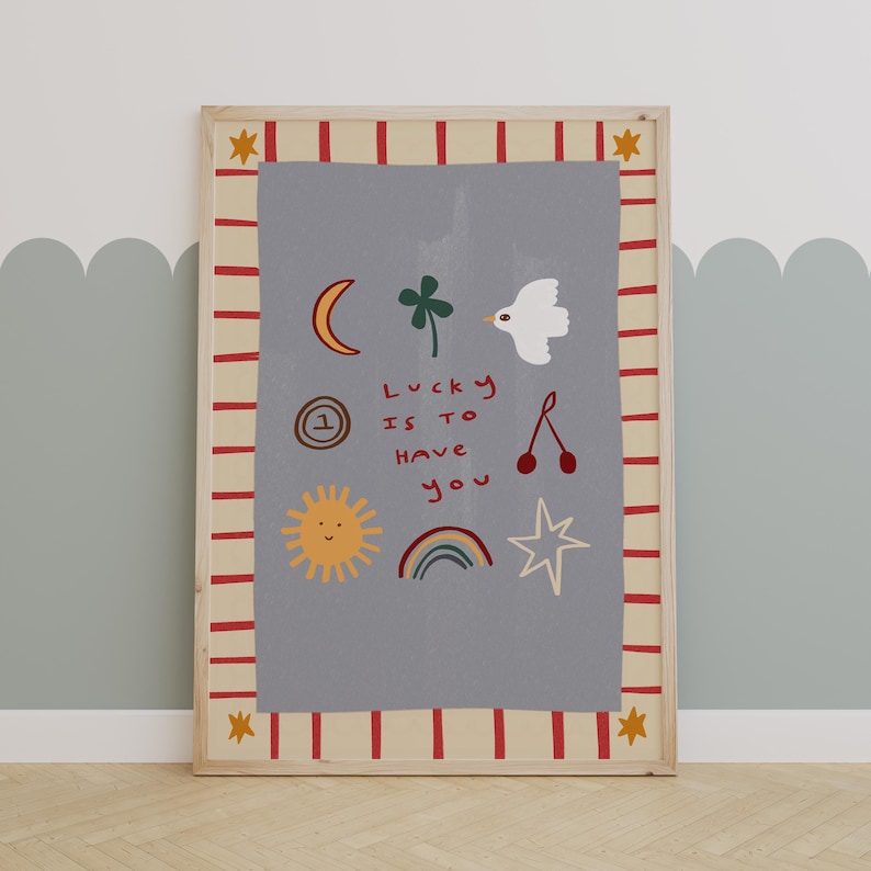 May include: A framed print with a light gray background and a red and white striped border. The print features a variety of hand-drawn illustrations, including a sun, a rainbow, a star, a clover, a bird, a crescent moon, a cherry, and a clock. The text "Lucky is to have you" is written in black.