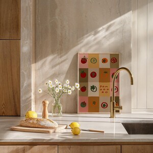 May include: A kitchen scene featuring a framed print with tomato illustrations, a bouquet of daisies in a glass vase, and a loaf of bread on a wooden cutting board. A gold faucet and lemons are also visible.