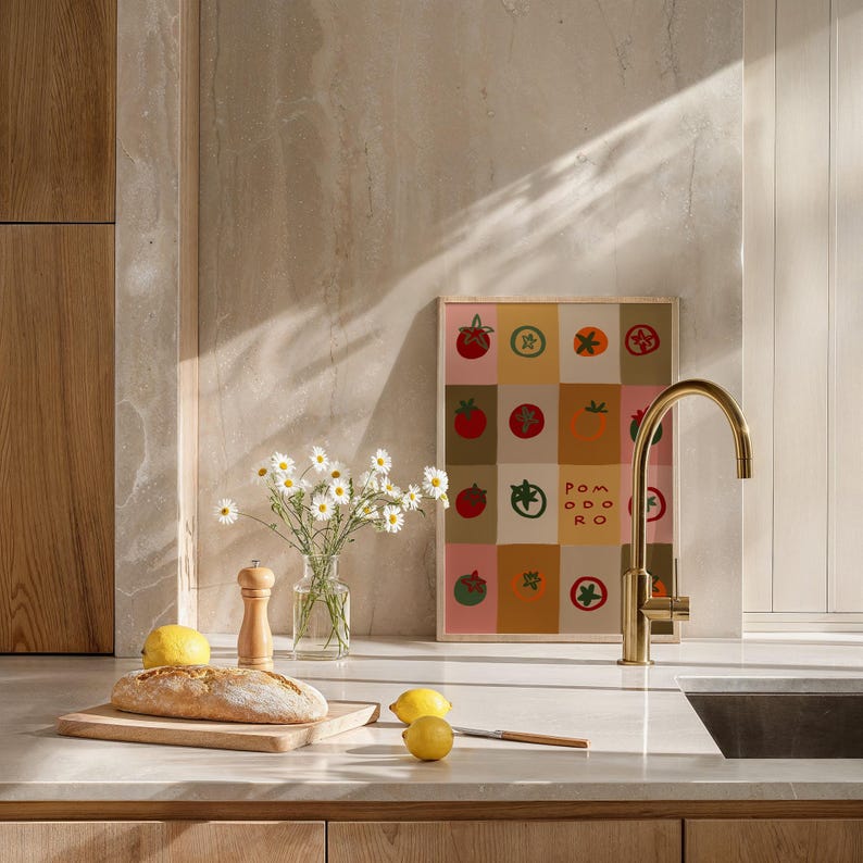 May include: A kitchen scene featuring a framed print with tomato illustrations, a bouquet of daisies in a glass vase, and a loaf of bread on a wooden cutting board. A gold faucet and lemons are also visible.