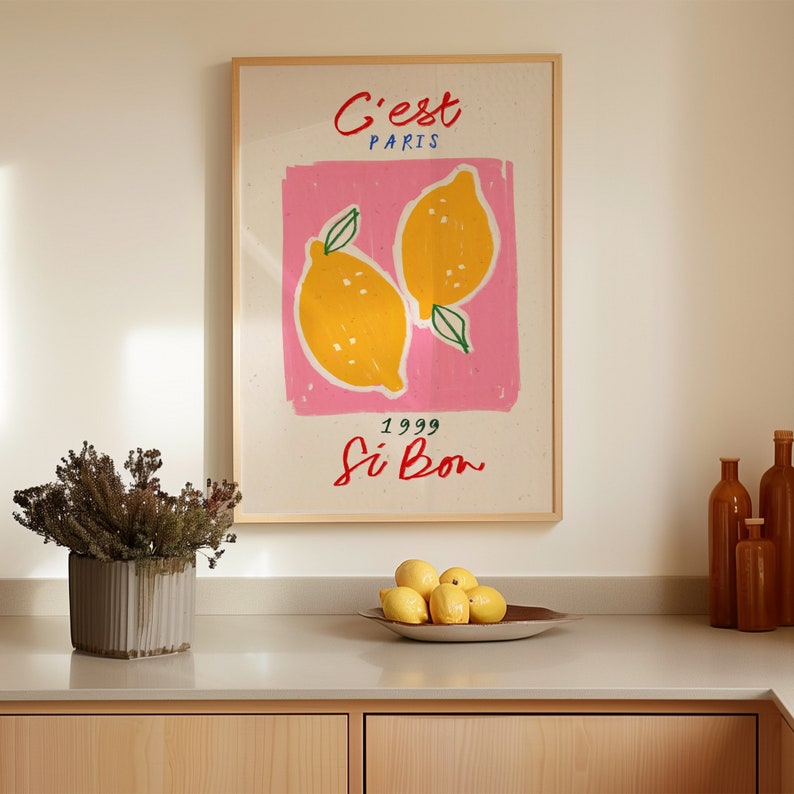 May include: A white poster with a pink rectangle in the center. The rectangle has two yellow lemons with green leaves. The poster says "C'est Paris 1999 Si Bon" in colorful lettering.