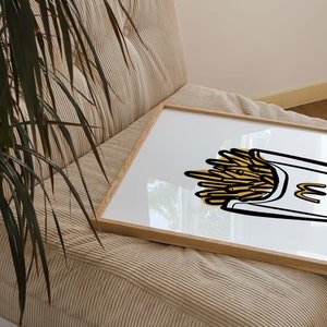 K&ouml;nnte beinhalten: Eine gerahmte Illustration einer gelben und wei&szlig;en Cartoon-Zeichnung einer Schachtel Pommes Frites. Die Schachtel tr&auml;gt den Buchstaben "M".