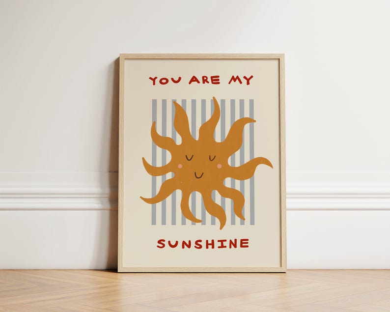 May include: A framed art print featuring a smiling, cartoon sun in shades of orange and yellow. The sun is set against a backdrop of vertical gray and white stripes. The words "YOU ARE MY SUNSHINE" are written in red.