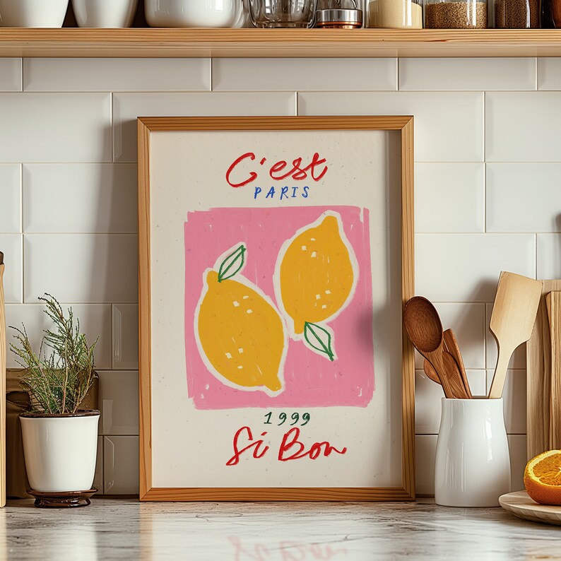 May include: A framed print with a pink background and two yellow lemons with green leaves. The text on the print reads "C'est Paris 1999 Si Bon".