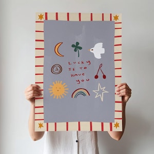 May include: A light blue poster with a red and white striped border. The poster features a variety of hand-drawn illustrations, including a crescent moon, a four-leaf clover, a white dove, a sun with a smiling face, a rainbow, a star, a cherry, and a number one inside a circle. The text on the poster reads "Lucky is to have you".