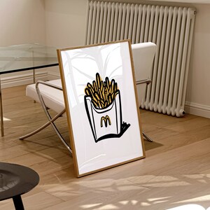 K&ouml;nnte beinhalten: Eine gerahmte Illustration eines wei&szlig;en Papierbeutels mit gelber Umrandung, gef&uuml;llt mit gelben Pommes Frites. Der Beutel hat einen schwarzen Umriss und ein schwarzes "M"-Logo.