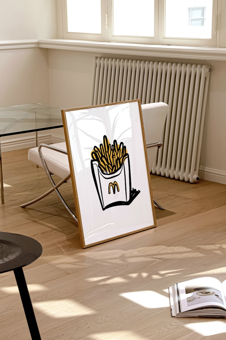K&ouml;nnte beinhalten: Eine gerahmte Illustration eines wei&szlig;en Papierbeutels mit gelber Umrandung, gef&uuml;llt mit gelben Pommes Frites. Der Beutel hat einen schwarzen Umriss und ein schwarzes "M"-Logo.