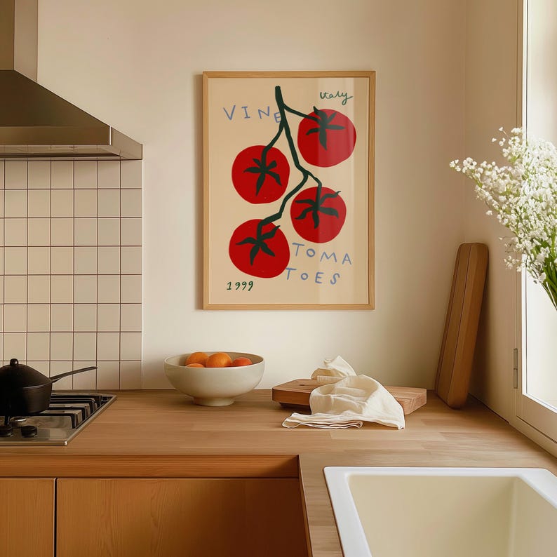 May include: A framed print of a red tomato vine with the text "VINE TOMATOES Italy 1999" in blue and purple lettering. The print is hanging on a beige wall in a kitchen.
