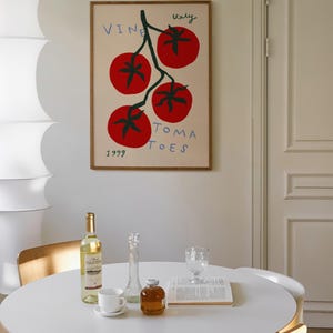 May include: A framed illustration of a tomato vine with four red tomatoes and the text "VINE ITALY TOMATOES 1999". The illustration is on a white background and is hanging on a white wall. A white table with a bottle of wine, a glass, a vase, and a book is in the foreground.