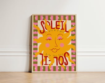 May include: A framed art print featuring a smiling sun illustration. The sun is yellow with pink cheeks and eyelashes. The word "SOLEIL" is at the top in red, and "like the sun" is below. The background has a pink and green checkered pattern.