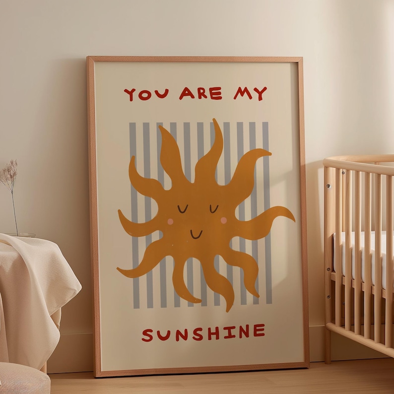 May include: A framed art print featuring a smiling sun illustration in shades of orange and yellow. The print has the words "YOU ARE MY SUNSHINE" in red. The background has vertical gray and white stripes.