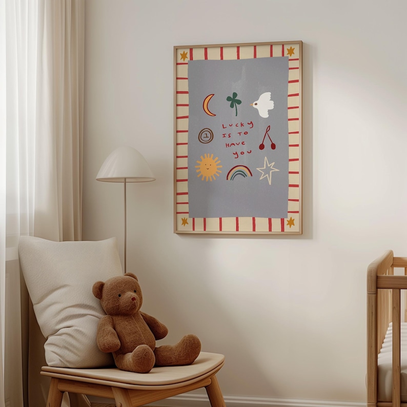 May include: A framed print with a light blue background and red and white stripes around the border. The print features a variety of hand-drawn illustrations, including a sun, a rainbow, a star, a clover, a bird, a crescent moon, and two cherries. The text "Lucky is to have you" is written in black.