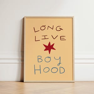 Könnte beinhalten: Ein gerahmter Kunstdruck mit den Worten "LONG LIVE BOY HOOD" im handschriftlichen Stil. Der Text ist in Dunkelrot und Blau auf hellorangefarbenem Hintergrund gehalten. Ein roter Stern befindet sich zwischen "LIVE" und "BOY". Der Rahmen ist hell.