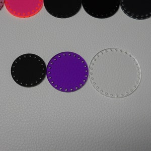 May include: A collection of circular craft pieces in various colors. The pieces include black, purple, and clear acrylic circles, each with evenly spaced holes around the perimeter. Other colors include pink and orange.