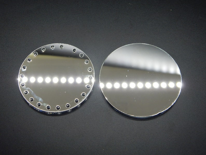 Puede incluir: Dos superficies redondas, de color plateado y reflectantes. Una superficie tiene un borde decorativo de peque&ntilde;os puntos negros espaciados uniformemente. Ambas superficies reflejan una fila de luces blancas.