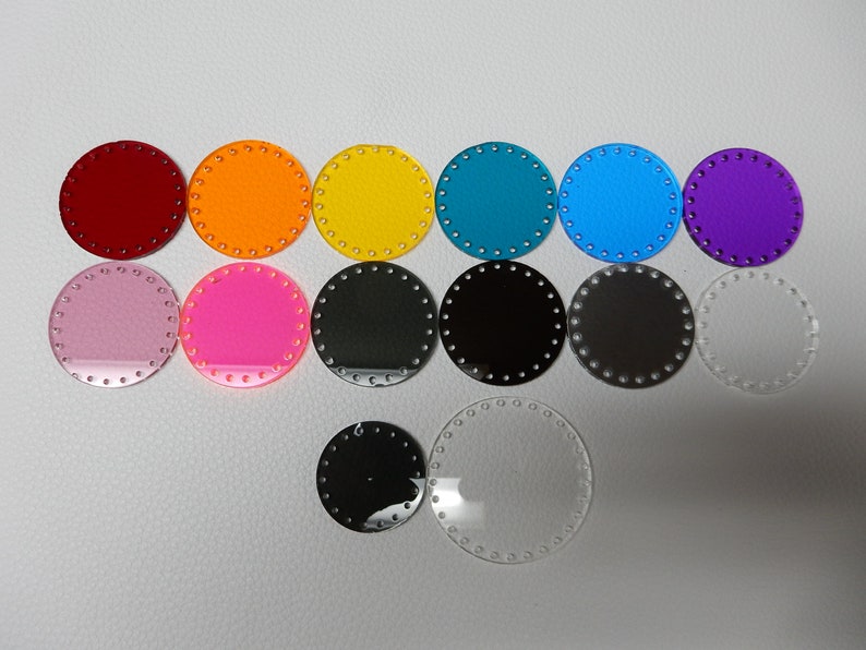 May include: A collection of colorful, round acrylic bases for crafting projects. The bases are available in various colors, including red, orange, yellow, teal, blue, purple, pink, black, gray, and clear. Each base has evenly spaced holes around the perimeter.