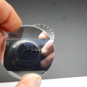 Puede incluir: Una lente redonda de vidrio transparente con una serie de peque&ntilde;os agujeros alrededor del borde. La lente refleja un objetivo de c&aacute;mara.