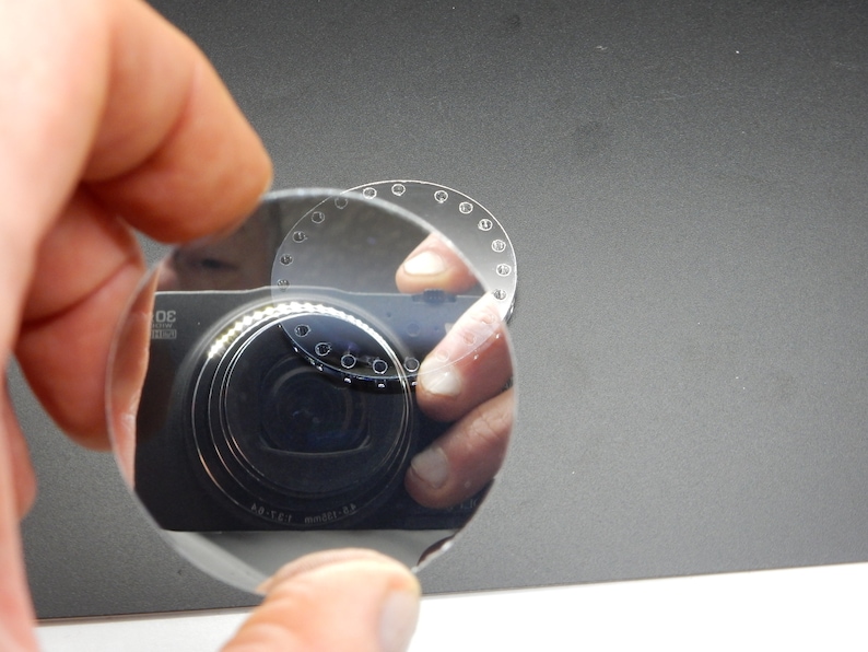 Puede incluir: Una lente redonda de vidrio transparente con una serie de peque&ntilde;os agujeros alrededor del borde. La lente refleja un objetivo de c&aacute;mara.