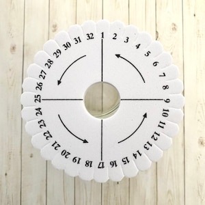 May include: White circular gauge with black numbers and arrows. The numbers range from 1 to 32. The gauge is used for measuring the size of beads.