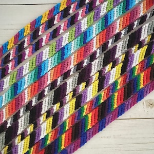 May include: A collection of colourful friendship bracelets made with embroidery floss. The bracelets are arranged in a diagonal pattern on a white wooden surface.