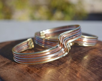 Peut inclure: Deux bracelets ondulés en cuivre avec des accents dorés. Les bracelets sont empilés l'un sur l'autre.