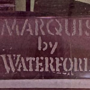 May include: A close-up of a dark purple surface with the words "MARQUIS by WATERFORD" in white, stencil-style lettering. The text is slightly blurred.
