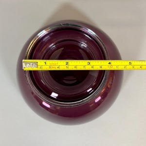 May include: A deep purple glass bowl with a silver rim, viewed from above. A yellow tape measure is placed across the bowl, showing a diameter of approximately 4 inches. The bowl has a rounded shape and a glossy finish.