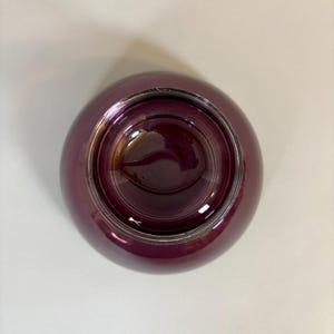 May include: A deep burgundy-colored glass bowl with a rounded shape. The bowl has a glossy finish and a silver-colored rim. The interior of the bowl is a darker shade of burgundy, creating a contrast with the exterior.