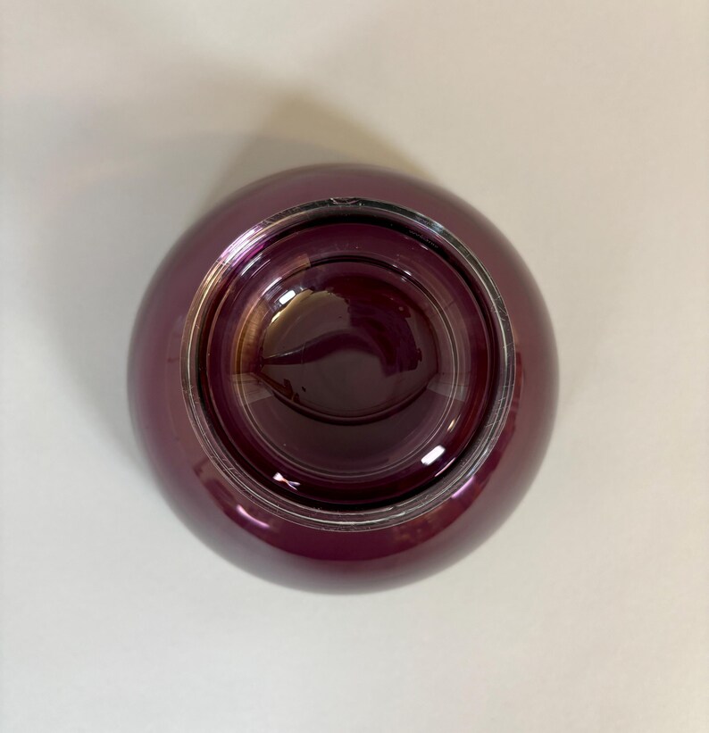 May include: A deep burgundy-colored glass bowl with a rounded shape. The bowl has a glossy finish and a silver-colored rim. The interior of the bowl is a darker shade of burgundy, creating a contrast with the exterior.