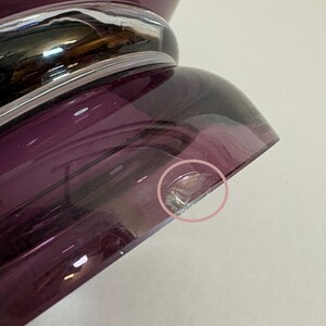 May include: Close-up of a purple glass vase with a silver band. The vase has a rounded base and a flared top. The glass has a glossy finish and a slight imperfection on the edge.