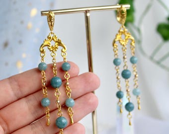 May include: Gold-toned chandelier earrings with aquamarine-colored beads. The earrings feature an ornate filigree design at the top, with multiple strands of beads suspended from delicate chains. The beads are round and vary slightly in size.