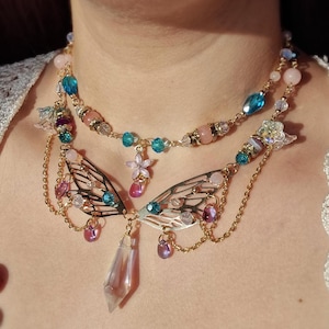May include: A layered gold necklace with a crystal pendant and delicate butterfly wings. The necklace features pink, blue, and purple beads, as well as clear crystals.