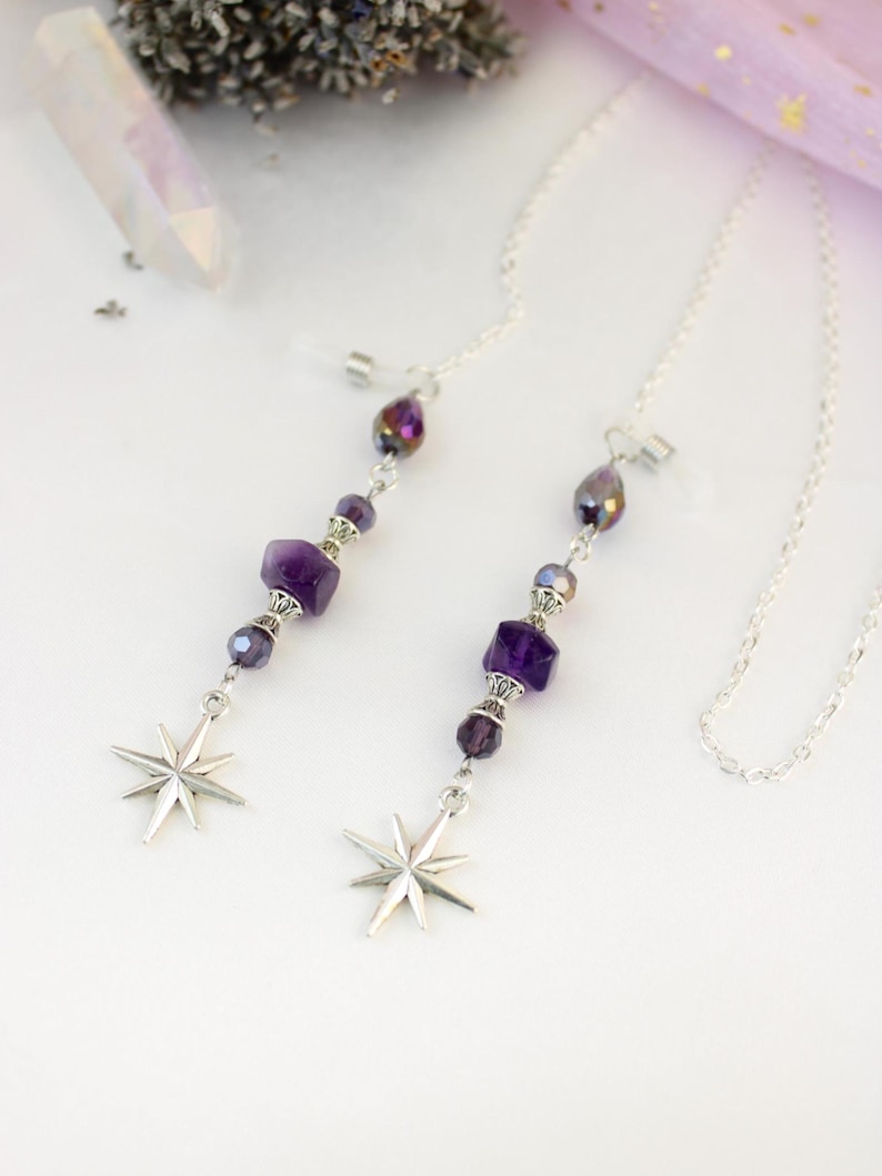 May include: Two silver eyeglass chains with purple amethyst beads and starburst charms. The chains have a delicate design with faceted beads and a teardrop-shaped bead at the top. The starburst charms are silver and have eight points.