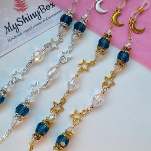 Könnte beinhalten: Brillenkette mit Himmelsmotiven. Die Ketten haben blaue Perlen, klare Kristallperlen und Stern- und Mondanhänger. Die Ketten sind in Silber- und Goldtönen erhältlich. Das Logo "MyShinyBox" ist im Hintergrund sichtbar.