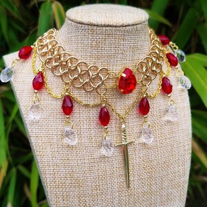 May include: A gold chainmail necklace with red and clear glass beads, a sword pendant, and a large red gemstone in the centre.
